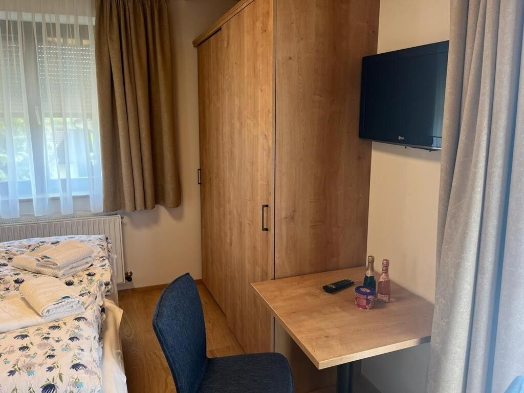 Een slaapkamer met een bed, een houten garderobe, een klein tafeltje met een afstandsbediening en een aan de muur bevestigde televisie.