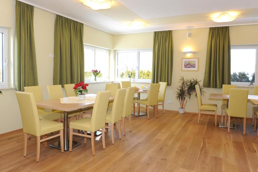 Un comedor con sillas amarillas y una mesa de madera, cortinas verdes y plantas en macetas.