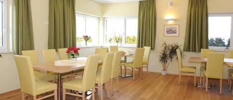 Un comedor con sillas amarillas y una mesa de madera, cortinas verdes y plantas en macetas.