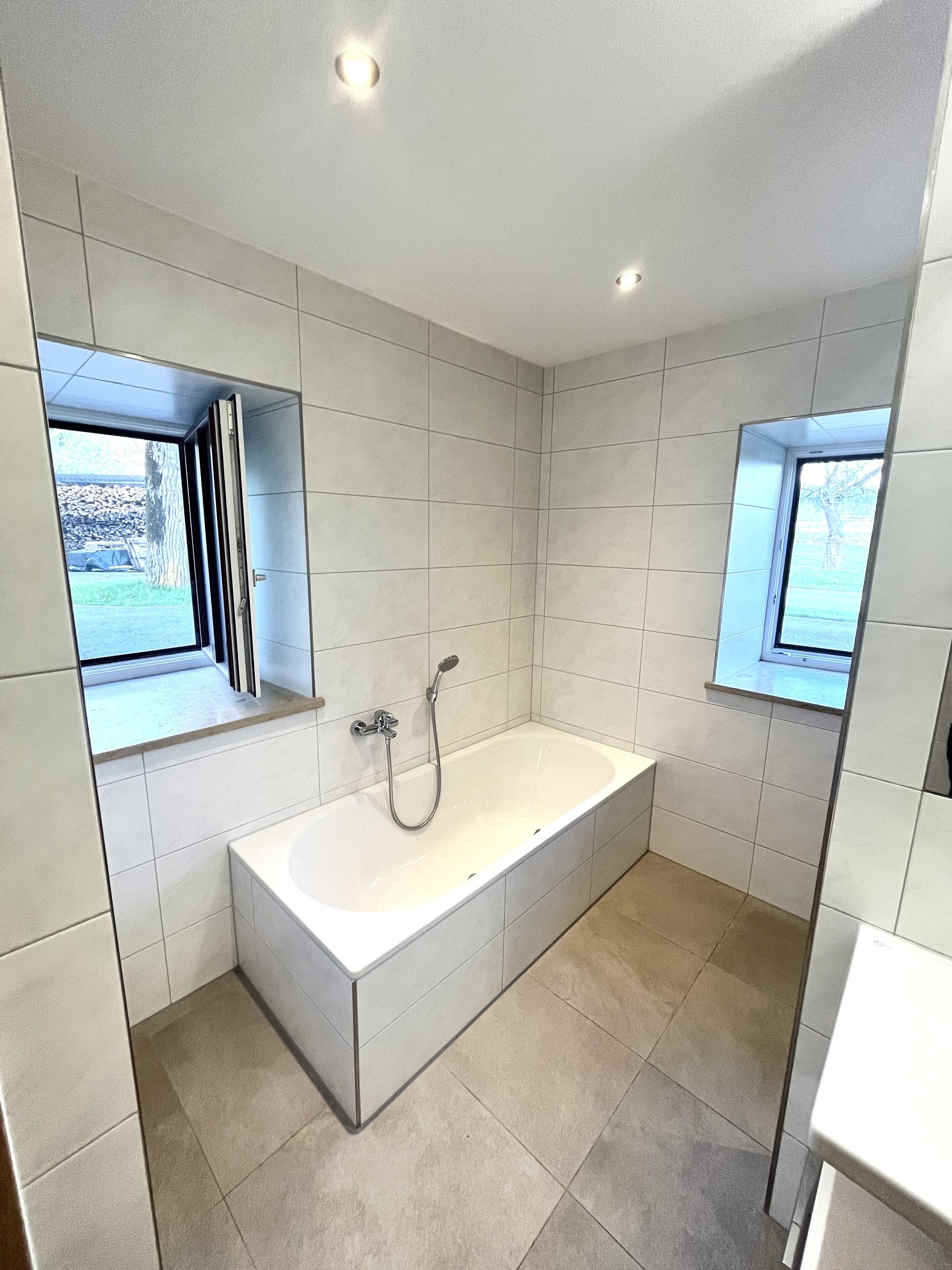 Un baño moderno con una bañera grande, dos ventanas y paredes con azulejos.
