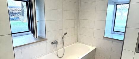 Un baño moderno con una bañera grande, dos ventanas y paredes con azulejos.