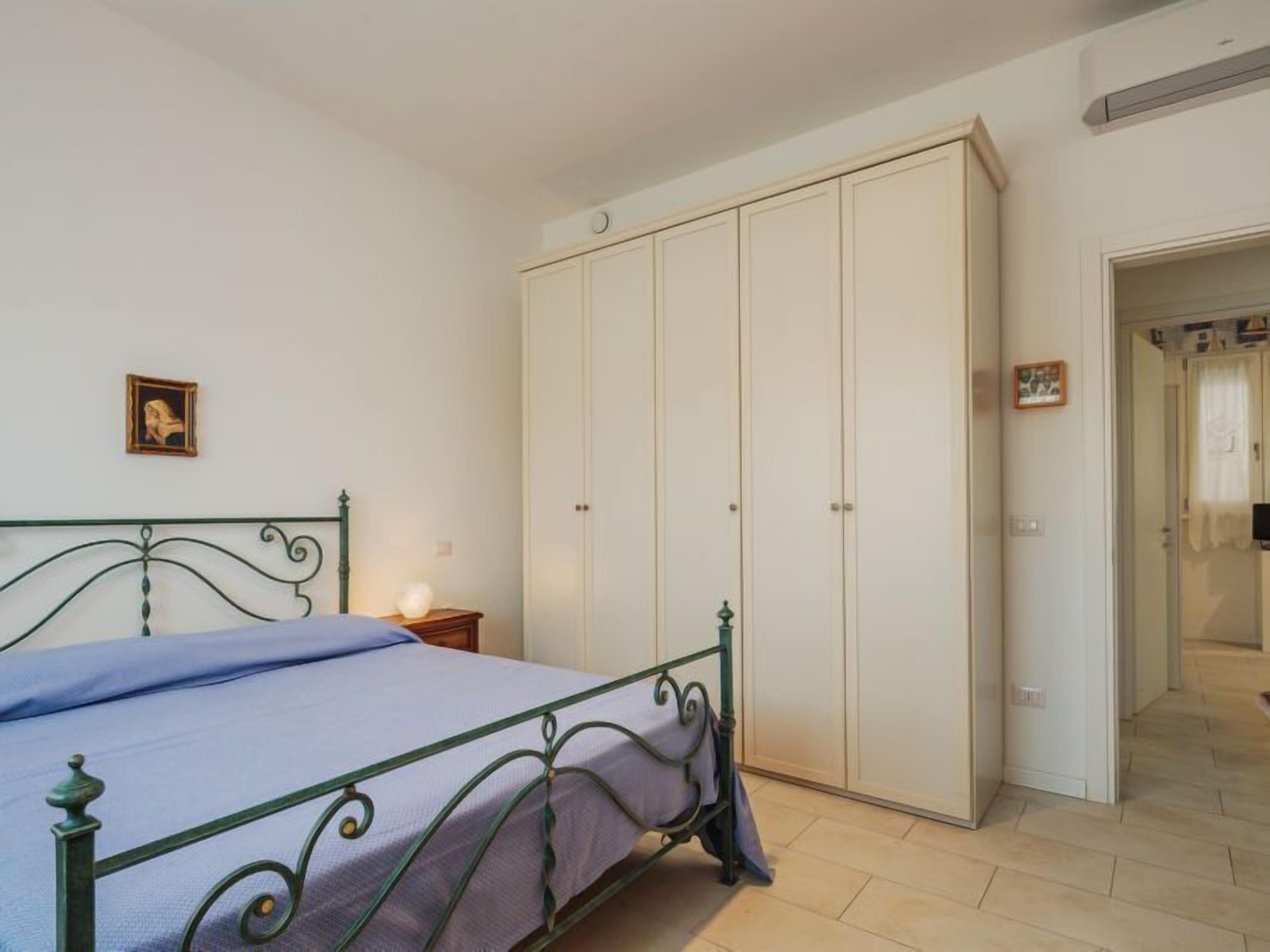 A bedroom with a bed, a wardrobe, a nightstand, and a framed picture on the wall.
