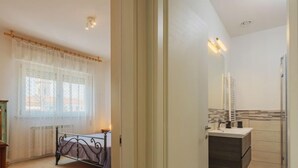 A bedroom with a bed, a window with curtains, and a bathroom with a sink and mirror. - Appartamento Maestrale by Interhome (Viareggio)