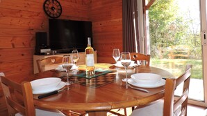 Een houten chalet inrichting met een eettafel voor vier personen, een televisie en een raam met uitzicht op groen.