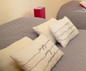 Deux oreillers ornés de motifs brodés, posés sur un lit recouvert d’une couverture matelassée grise.