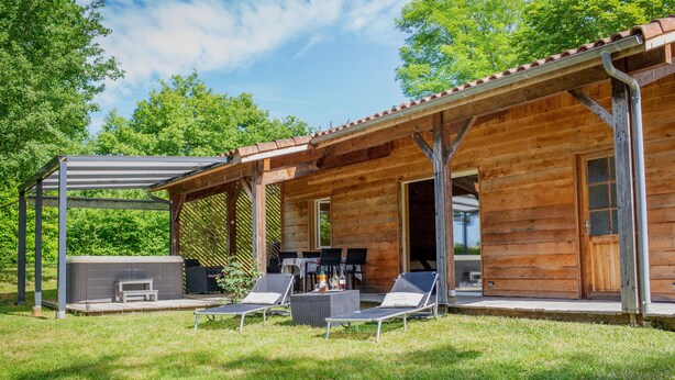 Een houten chalet met een overdekt terras, zitplaatsen buiten en een jacuzzi.