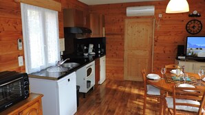 Een gezellige keuken met houten wanden, een eethoek met tafel en stoelen, een magnetron, een broodrooster en een kleine koelkast.