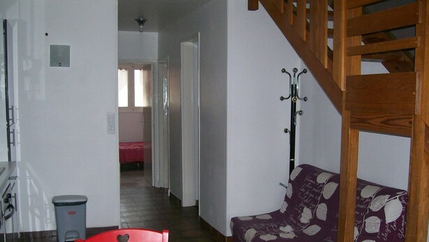 A cozy living room with a wooden dining table, red chairs, a patterned sofa, and a staircase.