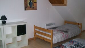 A bedroom with a wooden bunk bed, a white bedside table with a lamp, and a wall-mounted painting.