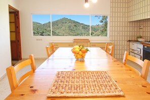 A dining area with a wooden table, chairs, a woven placemat, and a bowl of fruit.