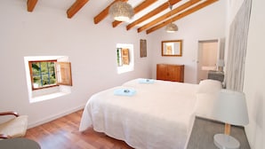 Une chambre à coucher avec un grand lit, des poutres en bois, une fenêtre, une table de chevet avec une lampe et une chaise.