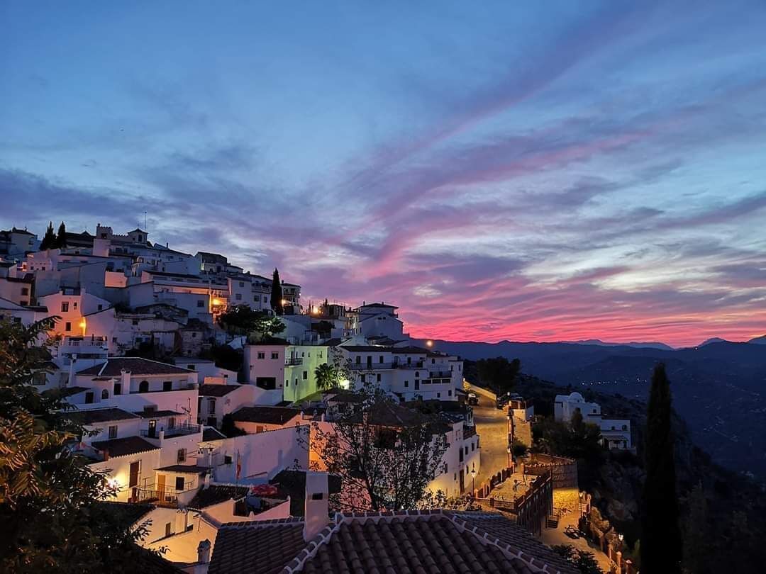 A coastal town at dusk with buildings illuminated, a prominent church, and a clear view of the sea.