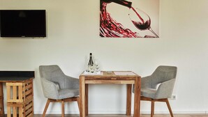 A dining area with a wooden table and two grey chairs, a television mounted on the wall, and a wine bottle and glasses on the table. - Appartment mit Panorama Blick (Stadecken-Elsheim)