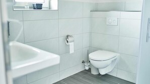 A modern bathroom with a toilet, sink, and a window above the sink. - Appartment mit Panorama Blick (Stadecken-Elsheim)