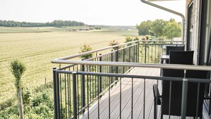 A balcony with a view of a green field, a metal railing, and a wicker chair. - Appartment mit Panorama Blick (Stadecken-Elsheim)