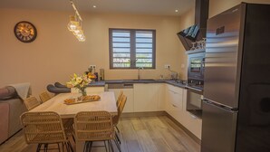 A modern kitchen with a dining area, featuring a large refrigerator, a built-in oven, and a window with blinds. - Charming villa between sea and mountains, ideal for friends or family (Saint-Louis)