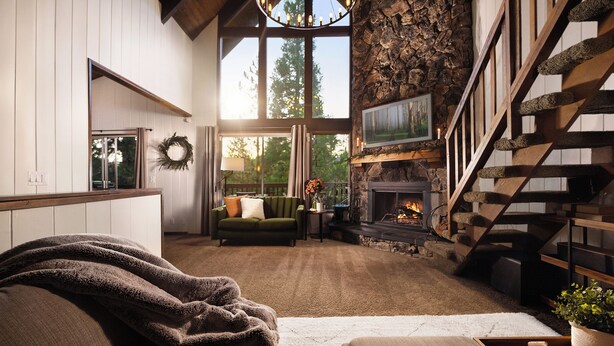 A spacious living room with a fireplace, a stone wall, and a wooden staircase.
