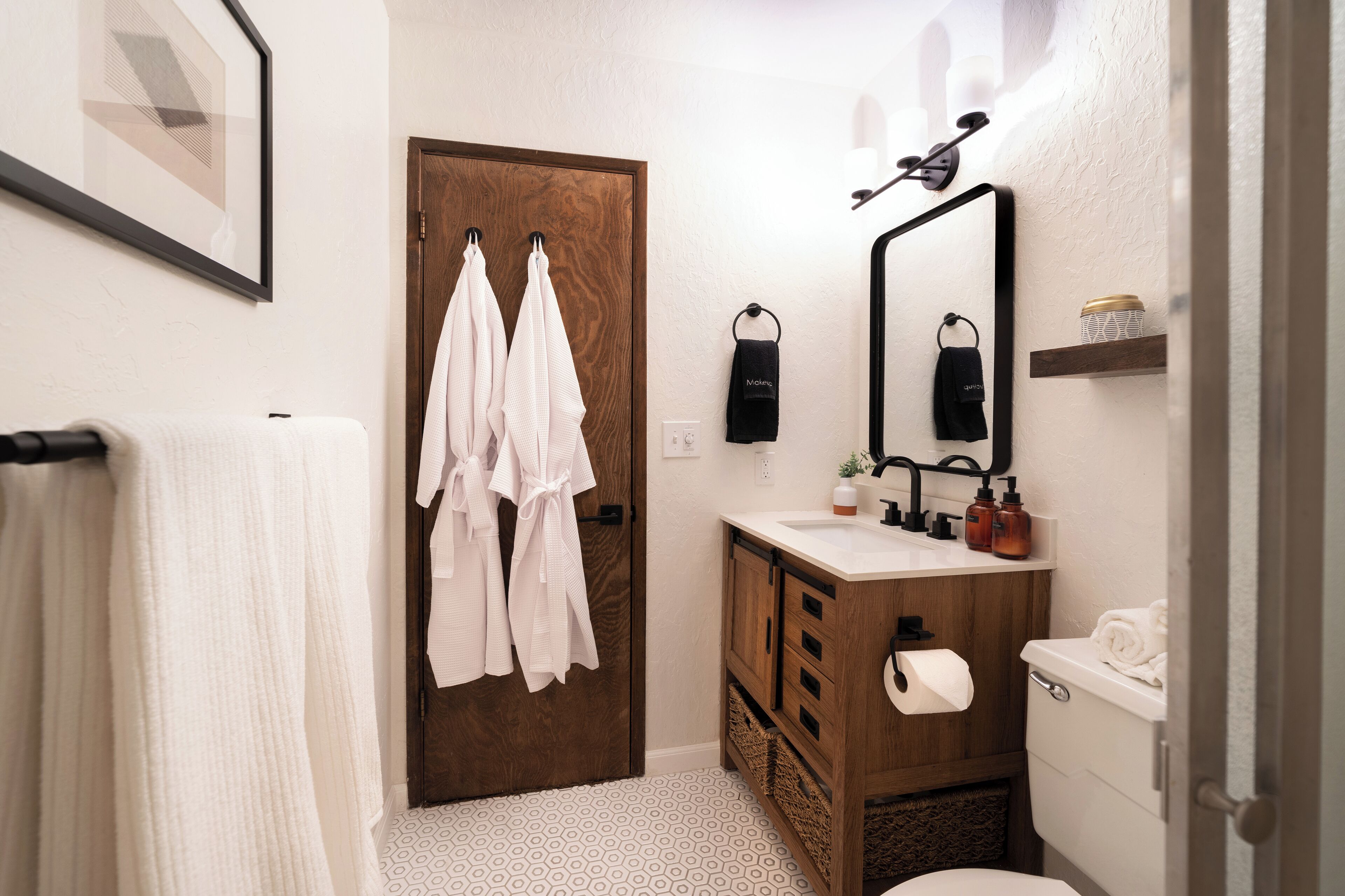 A bathroom with a wooden door, a white towel hanging on the wall, a sink with toiletries, and a toilet.