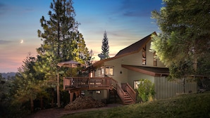 A two-story house with a wooden deck, a staircase, and a satellite dish.
