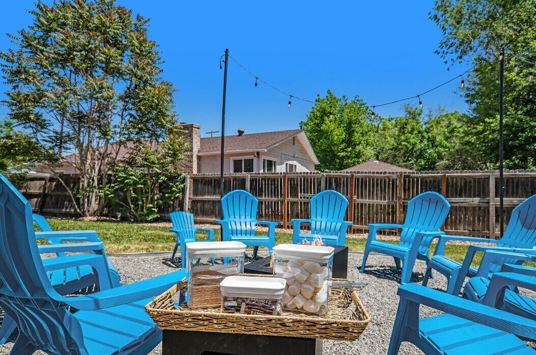 A backyard with blue Adirondack chairs arranged around a fire pit, a wooden table, and a basket.