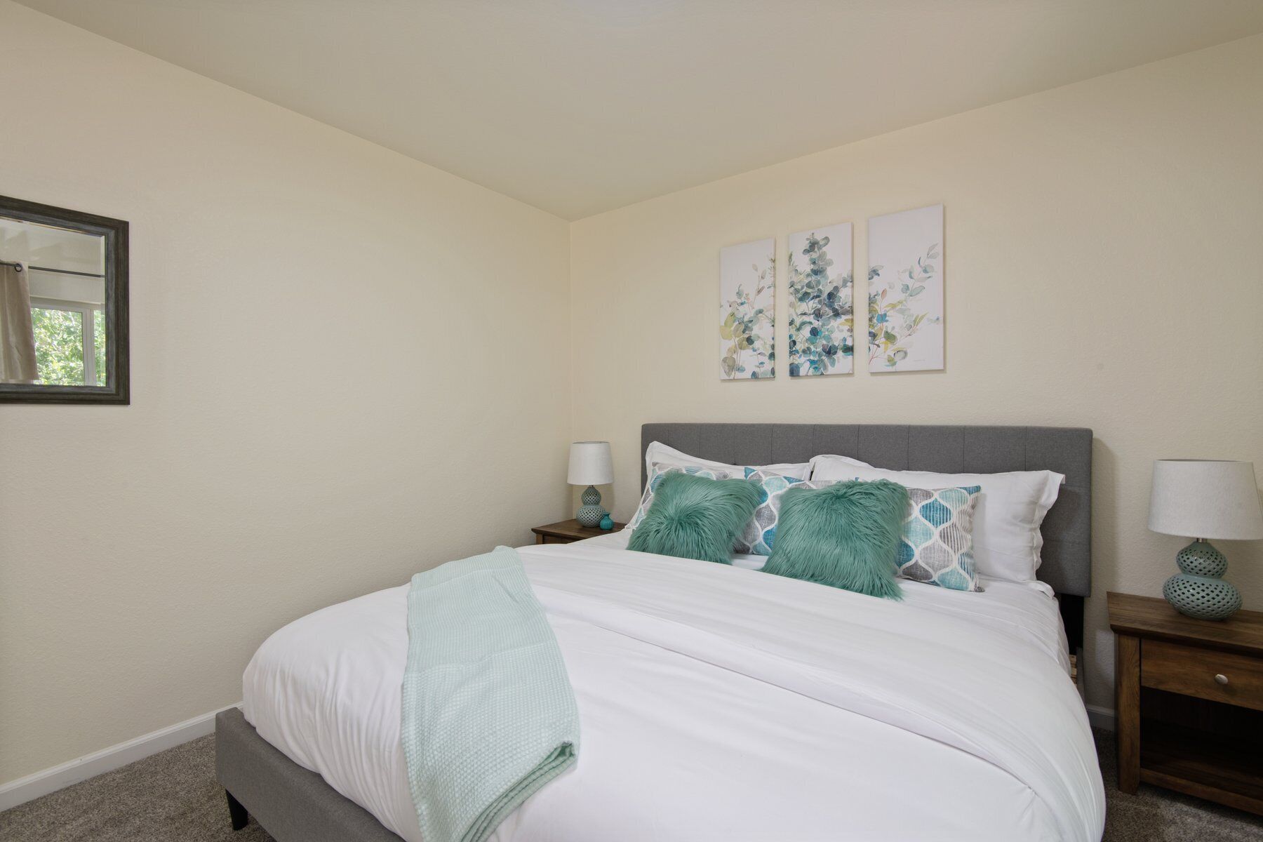 A bedroom with a bed, two nightstands, a window, and three wall-mounted artworks.