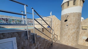 Un escalier extérieur mène à un espace piscine agrémenté d’un mur en pierre et d’une structure en forme de tour.