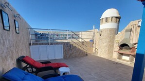Une terrasse sur le toit, dotée de chaises longues, d’un espace barbecue et d’un mur en pierre surmonté d’une structure en forme de dôme.