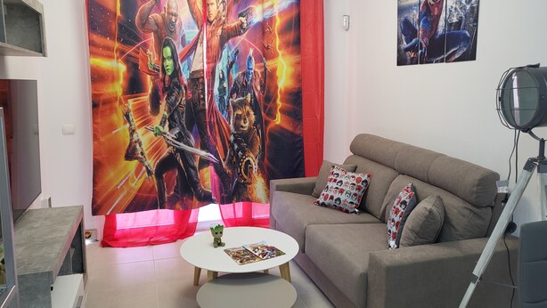 Un salon comprenant un canapé, une petite table ronde, un rideau rouge orné d’une affiche de film et un tableau accroché au mur.