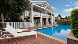 Ein modernes, zweistöckiges Haus mit Swimmingpool, einer Holzterrasse und einem weißen Zaun.