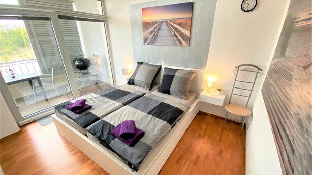 A modern bedroom with a large bed, a glass door leading to a balcony, and a painting of a sunset over a pier. - LUXURY Apartment 2 floors 3BR! +NETFLIX +HIGH-END (Ližnjan)