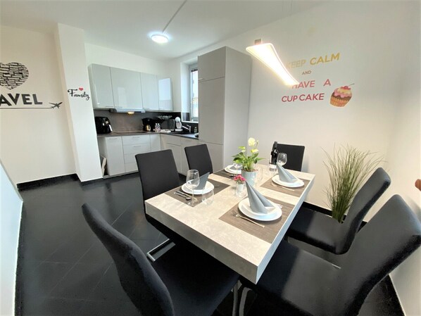 A modern dining area with a long table set for four, black chairs, and a decorative plant.