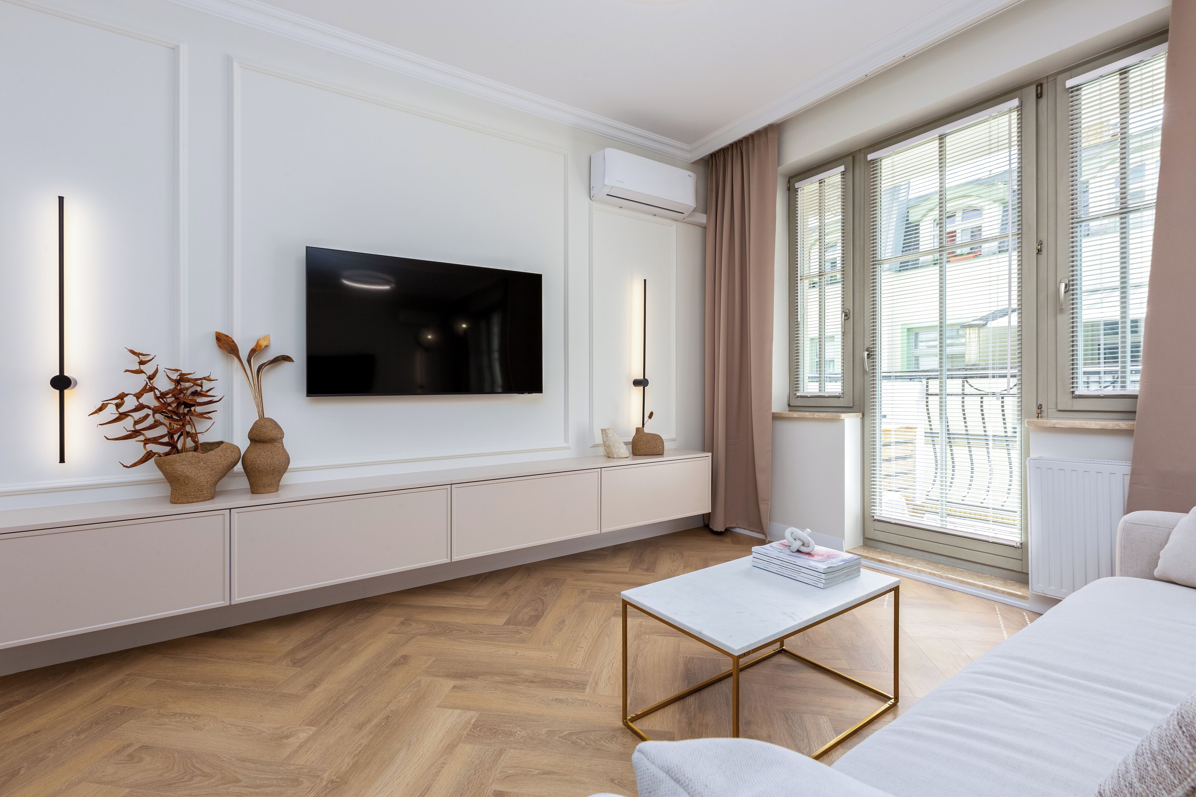 Un salon moderne avec un téléviseur à écran plat fixé au mur, un canapé, une table basse et une fenêtre équipée de stores.