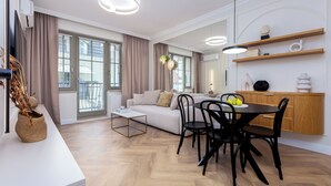 A modern living room with a sofa, dining table, and chairs. There is a kitchen area with wooden cabinets and a countertop.