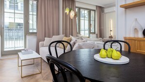 A modern living room with a dining table, a sofa set, and a large window with curtains.