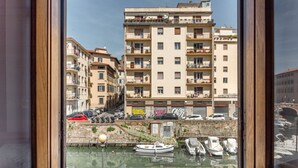 A view through a window of a building with multiple floors, balconies with plants, and a marina with boats. - GuestHost - Little Venice Charming Flat with Canal View (Livorno)