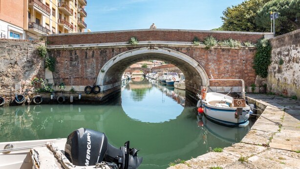 A canal with boats, a bridge, and a building with balconies. - GuestHost - Little Venice Charming Flat with Canal View (Livorno)