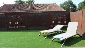 An outdoor area with artificial grass, two lounge chairs, and a wooden deck. - Gite Aramis (Les Herbiers)
