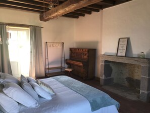 A bedroom with a bed, a wooden dresser, a hanging clothes rack, and a stone fireplace.