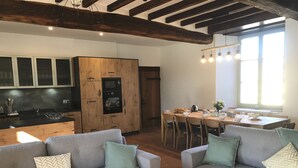 A modern kitchen with wooden cabinets, a dining area with a table and chairs, and a gray sofa with patterned cushions. - Gite Aramis (Les Herbiers)
