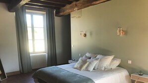 A bedroom with a large bed, a window with curtains, a radiator, and a wooden ceiling. - Gite Aramis (Les Herbiers)