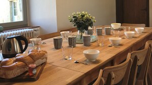 A long wooden dining table set with various bowls, glasses, and a loaf of bread. - Gite Aramis (Les Herbiers)