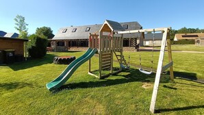 A playground with a slide and swings, surrounded by a grassy yard and a house with a sloped roof. - LONGERE NEAR HONFLEUR, DEAUVILLE, LE HAVRE (Beuzeville)