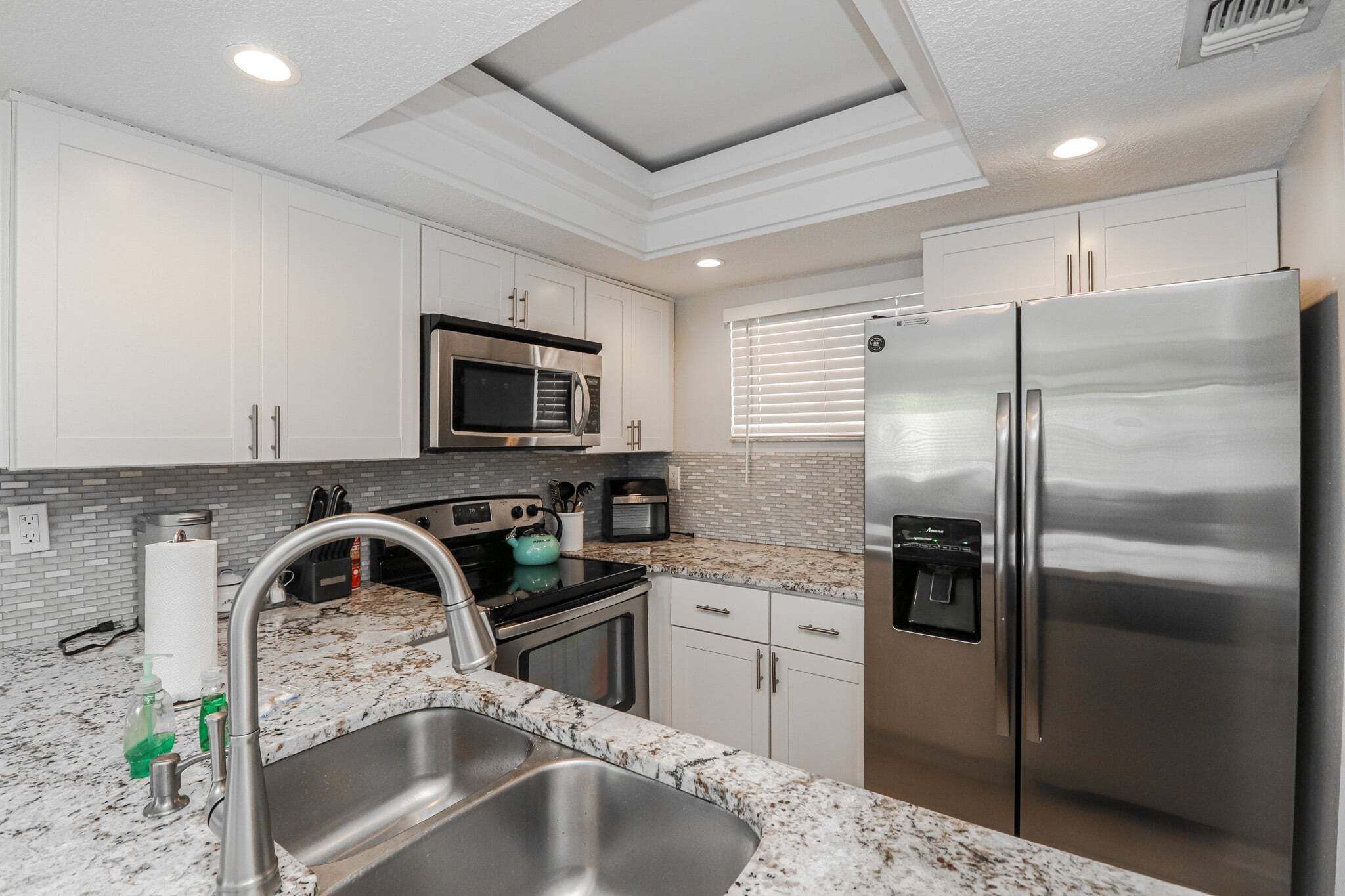 A modern kitchen with white cabinets, stainless steel appliances, a granite countertop, and a built-in water dispenser.