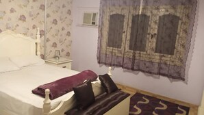 Un dormitorio con cama, mesita de noche, sofá, alfombra estampada y ventana con cortinas.