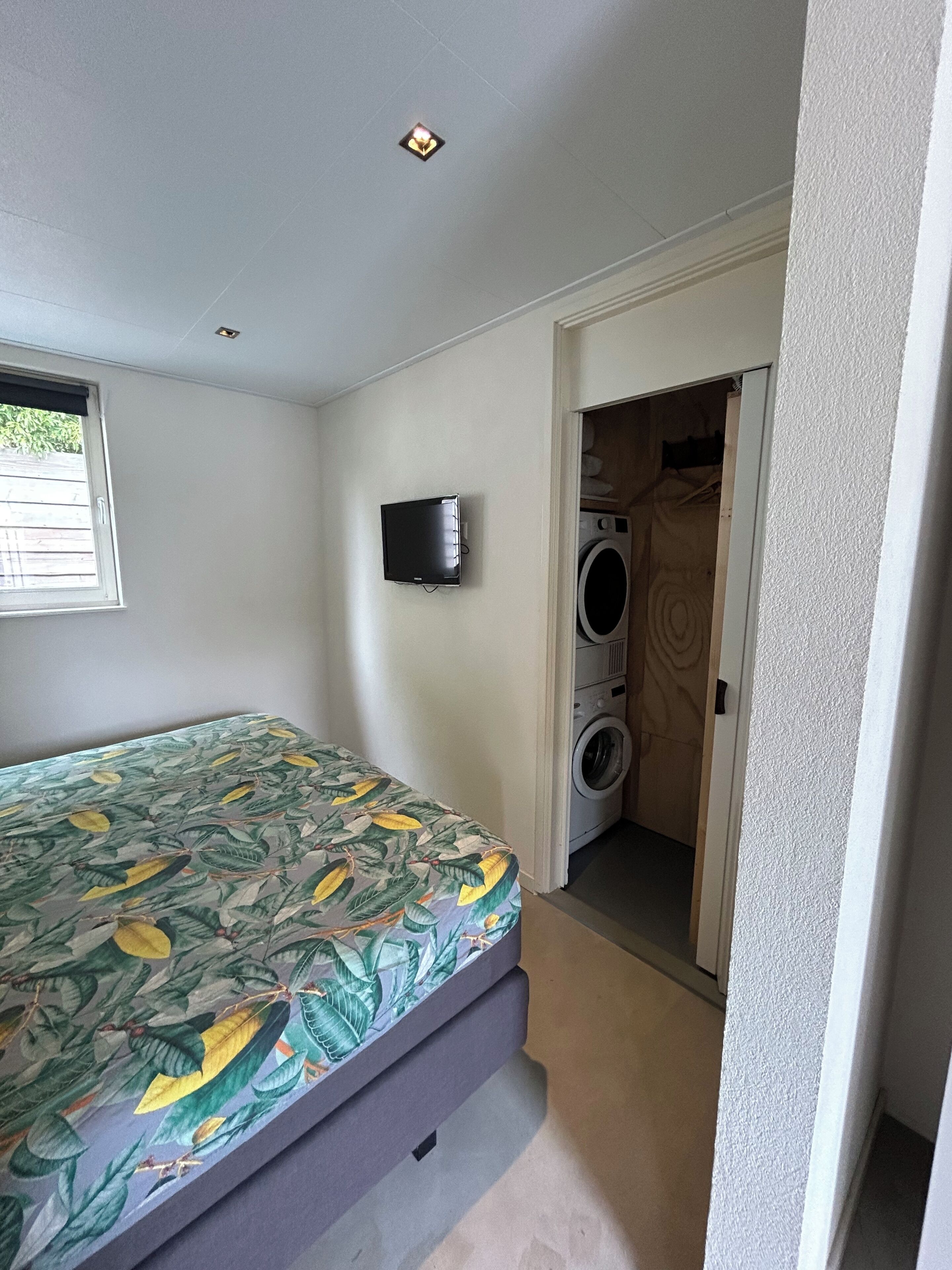 Une chambre à coucher avec un lit, une télévision et un lave-linge dans la pièce adjacente.