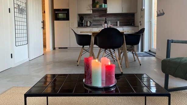 Una cocina moderna con armarios blancos, encimera negra y una zona de comedor con sillas negras.