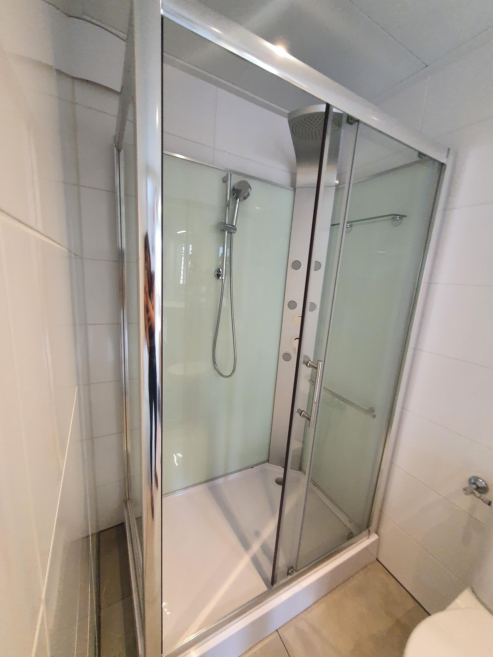 Cabina de ducha con paredes de vidrio, ducha de mano y grifo empotrado.