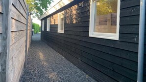 Un sendero estrecho que conduce a un edificio con revestimiento de madera oscura y ventanas con marco blanco.