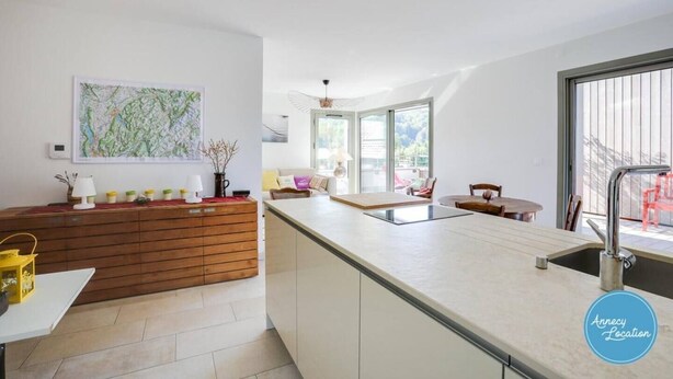 Una cocina moderna con una isla grande, un comedor con mesa y sillas, y vistas al exterior a través de amplios ventanales.