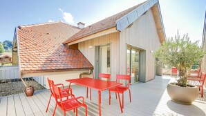 Una casa moderna con techo de tejas, un patio con mesa y sillas, y una planta grande en maceta.
